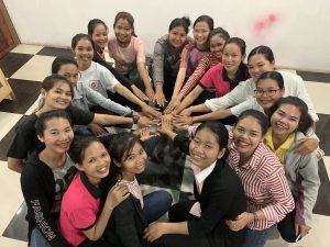 A group of young adult girls smiling and forming a circle with their hands