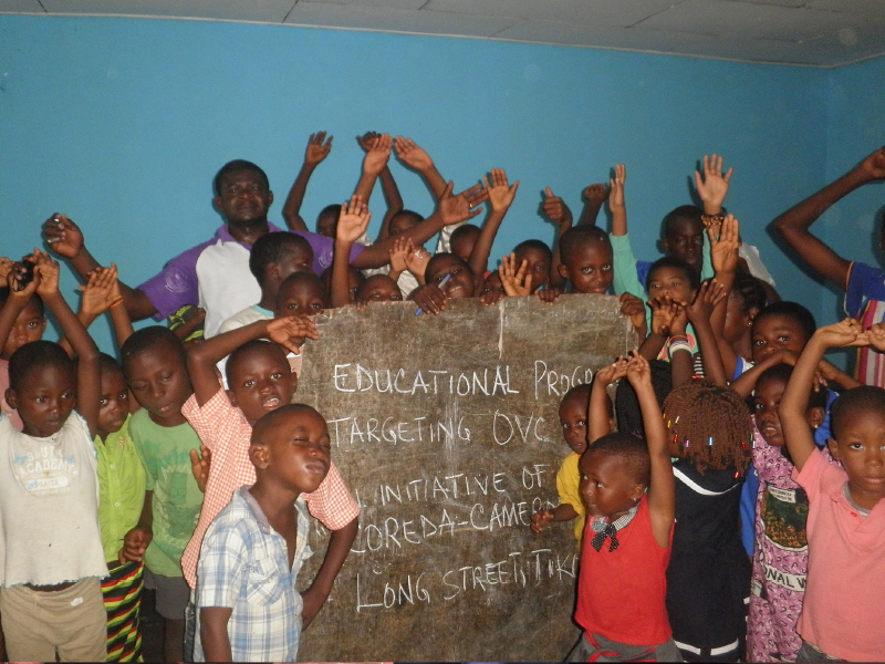 Group of children and adults smiling and raising hands inside a room.