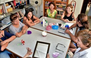 Five adults gathered around a table in a cozy room, engaging in an art or craft activity.