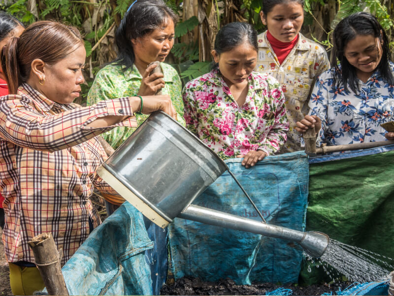 Women pouring liquid into a blue container outdoors.