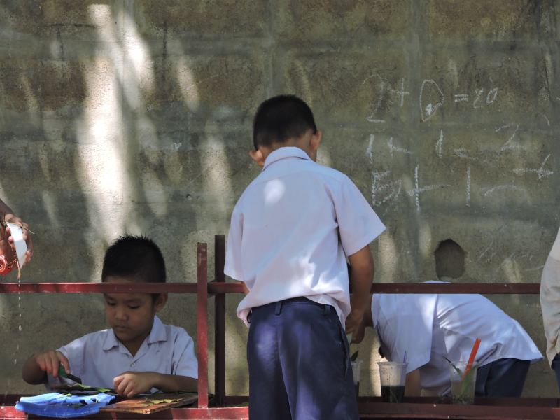 Children in school uniforms studying and writing outdoors near a brick wall. Children in school uniforms studying and writing outdoors near a brick wall.