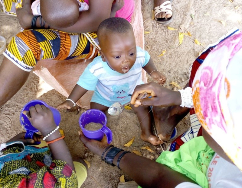 A child sitting among adults eating food from bowls.