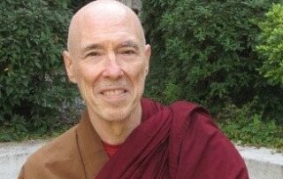 Smiling elderly monk in traditional robes outdoors.