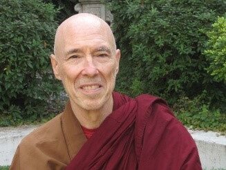 Smiling elderly monk in traditional robes outdoors.