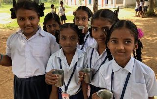 Group of school girls in uniforms holding metal cups, smiling outdoors.