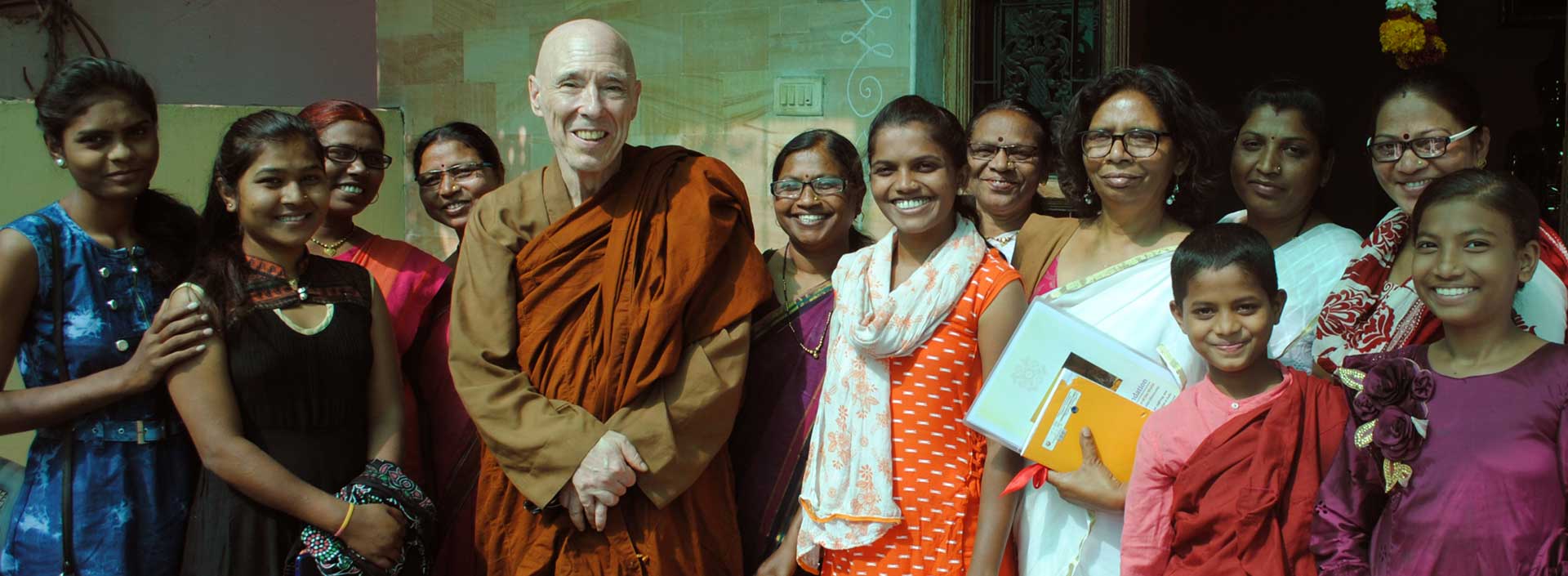 A monk smiling with three women, all posing for a photo indoors.
