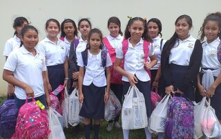 Group of smiling schoolgirls in uniforms holding bags.