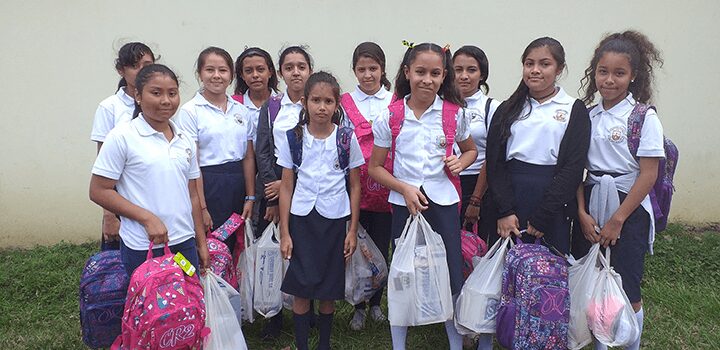 Group of smiling schoolgirls in uniforms holding bags.