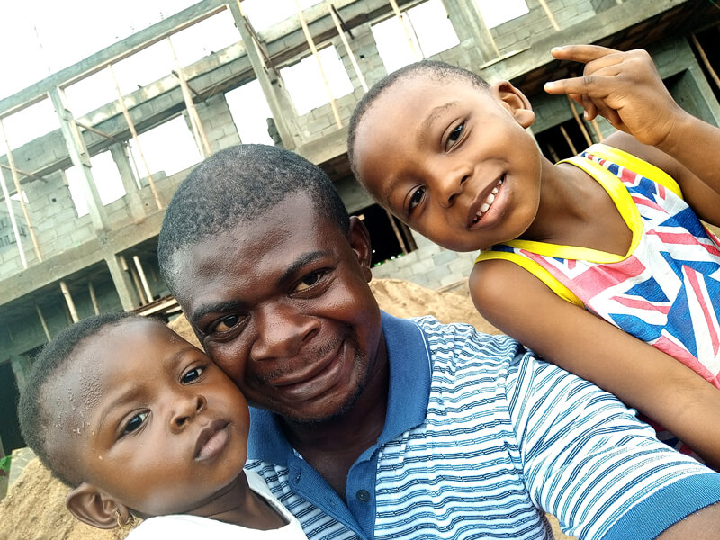 A man smiling with two young children outdoors.
