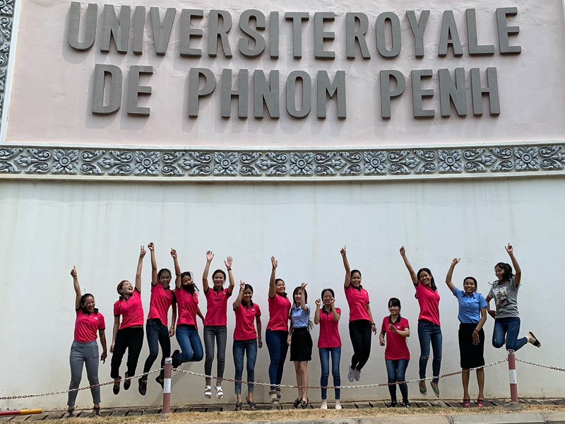 Group of students jumping in front of a university building with raised arms.