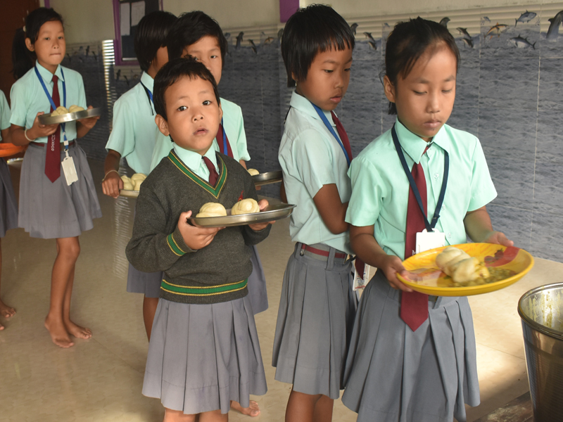 School children in uniforms holding plates of food in a queue.
