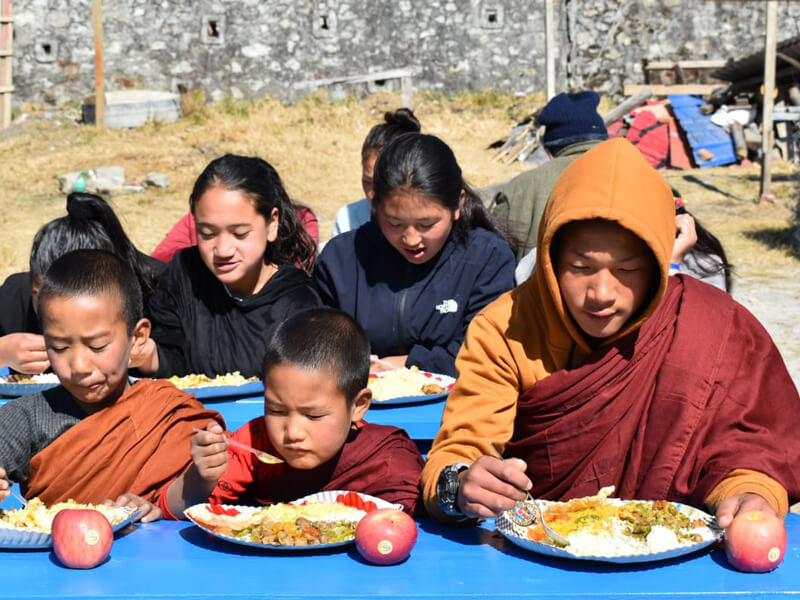 Children and monks eating together outdoors in a communal setting.