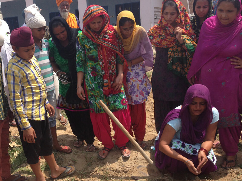 A group of women gathered outdoors, one stirring a pot with a stick.
