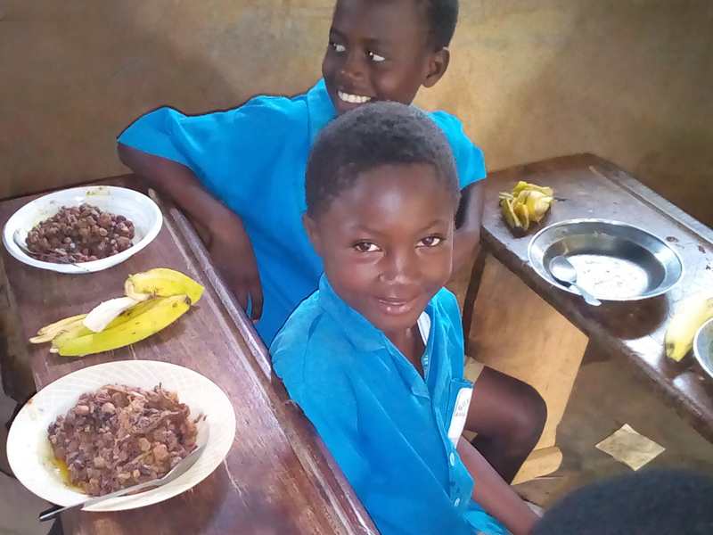 Two children in blue uniforms smiling at the camera during mealtime.