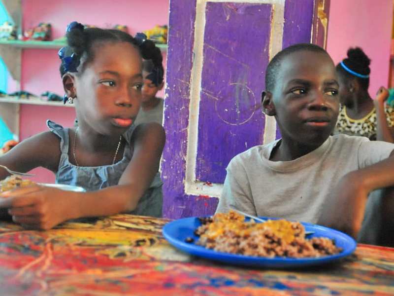Two children sitting at a colorful table with a plate of food.