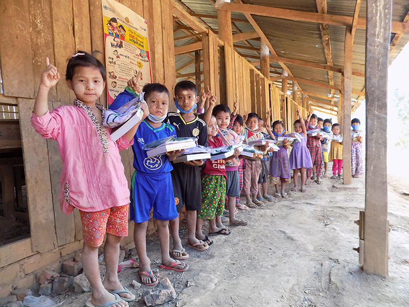 Children lined up holding plates of food in a wooden structure.