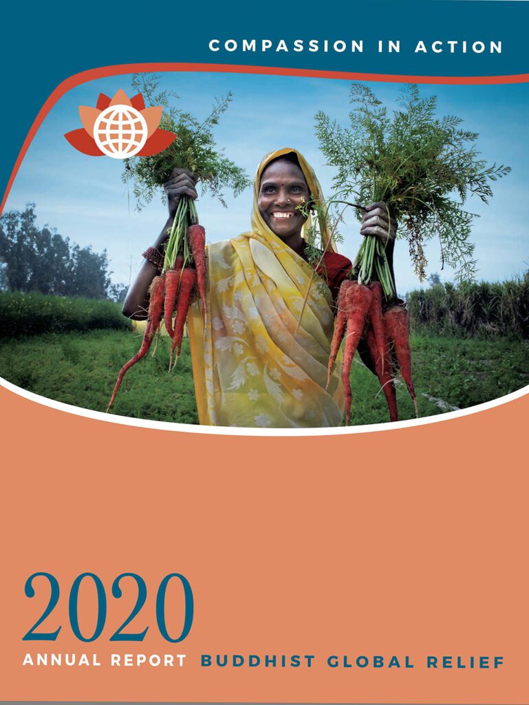 A smiling woman in a yellow sari holds fresh carrots in a rural setting.