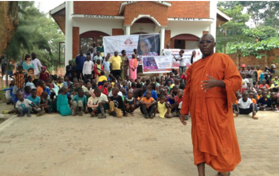 A group gathering with a monk in orange robes in the foreground.