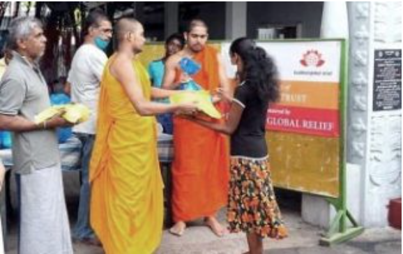 Monks handing out relief supplies to a woman during a community aid event.
