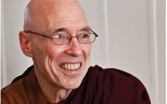 Smiling elderly man with glasses and a bald head.