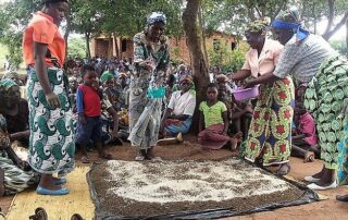 Community members gather outdoors, working on a craft project with natural materials.