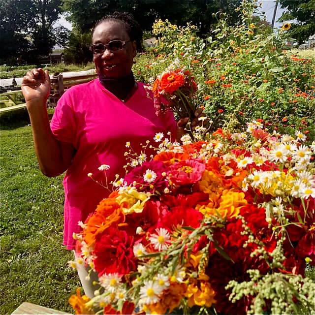 Woman in a pink dress holding flowers in a vibrant garden.