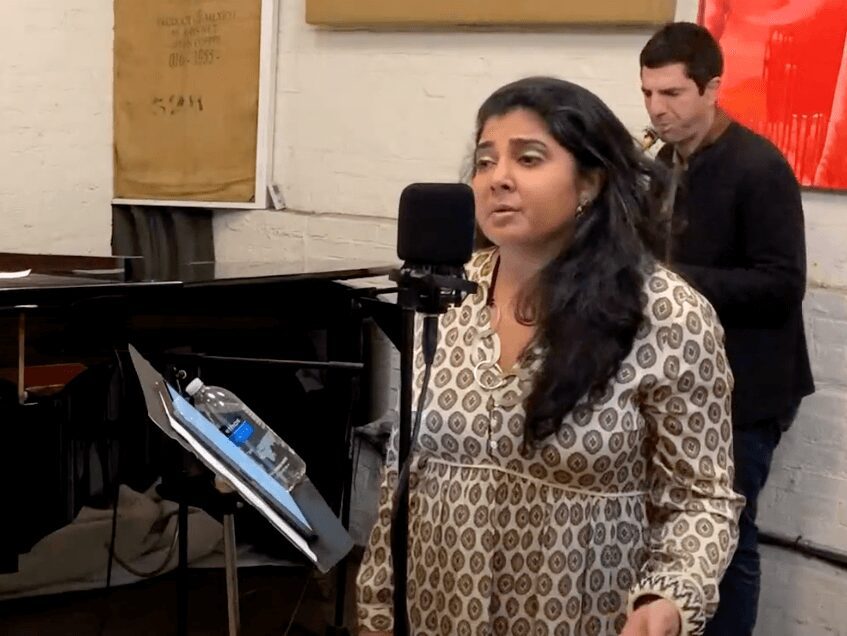 Woman singing in a music rehearsal room with a pianist in the background. Woman singing in a music rehearsal room with a pianist in the background.