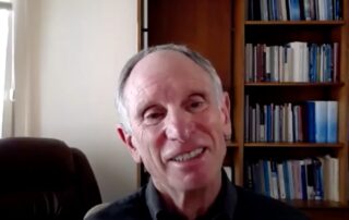 Smiling elderly man with bookshelves in the background.