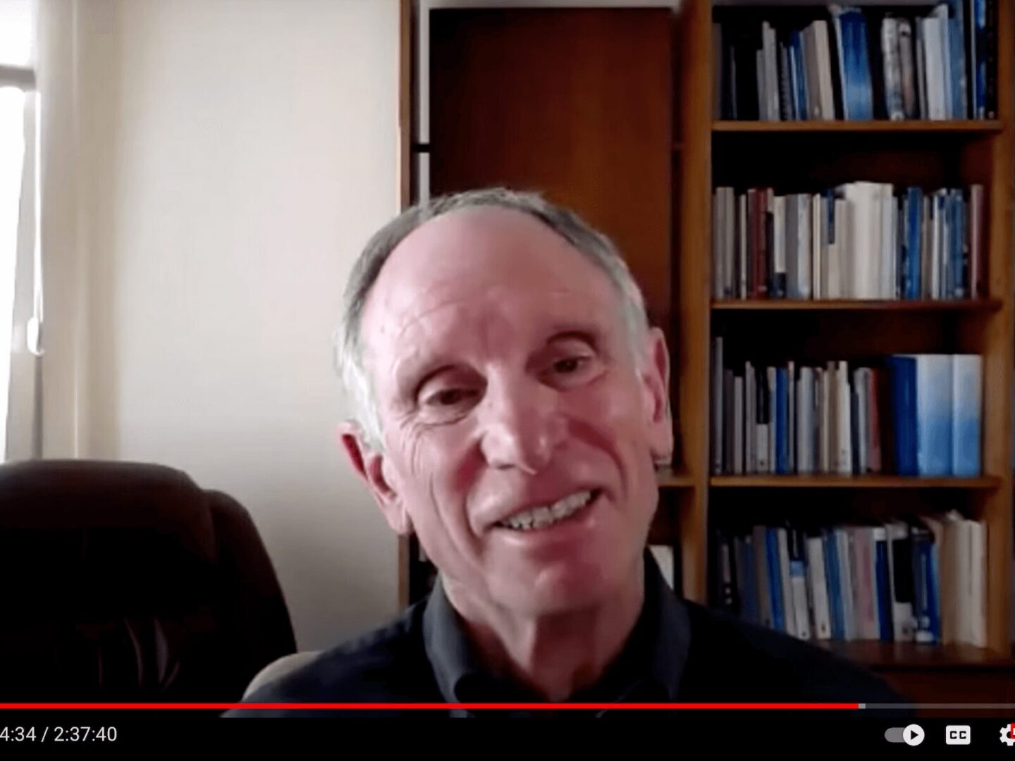 Smiling elderly man with bookshelves in the background.