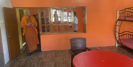 Woman in orange outfit standing near a large mirror in an orange-walled room.