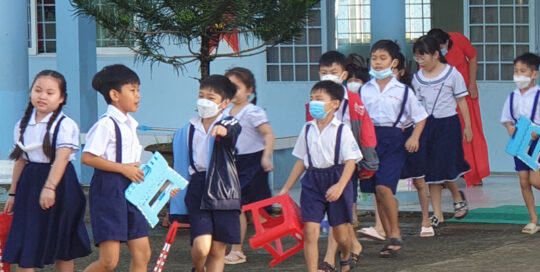 Young students in uniform walking outdoors, some wearing masks.