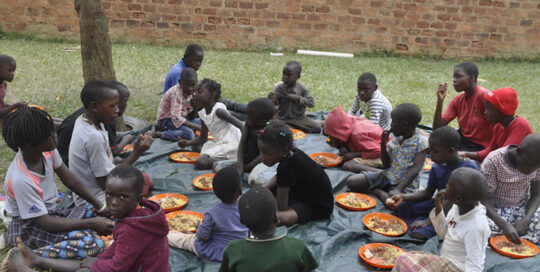 Children sharing a meal together outdoors on a mat.