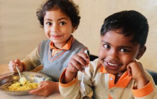 Two Sri Lankan children smiling and eating a healthy breakfast.