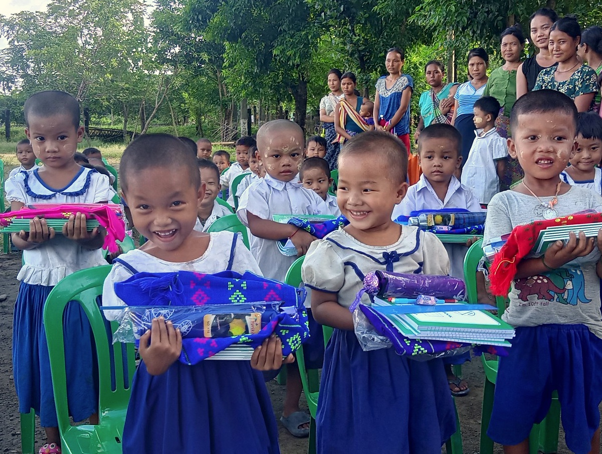 Smiling children in a Myanmar IDP camp show the camera their new schoolbooks.