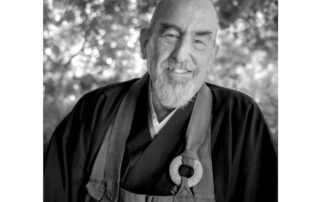 A serene elderly man in traditional robes smiles warmly outdoors.