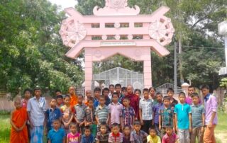 Group of children and adults posing under a decorative arch in a garden.
