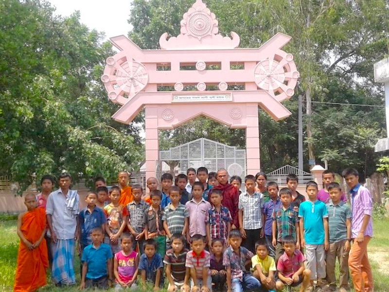 Group of children and adults posing under a decorative arch in a garden.