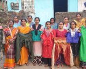 A group of women standing together, some holding shawls, outdoors in front of a building.
