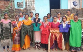 A group of women standing together, some holding shawls, outdoors in front of a building.