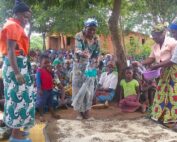 Women in colorful traditional attire dancing outdoors with a crowd watching.