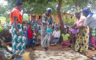 Women in colorful traditional attire dancing outdoors with a crowd watching.