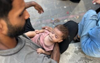 A man gently holds a sleeping baby in his arms outdoors.