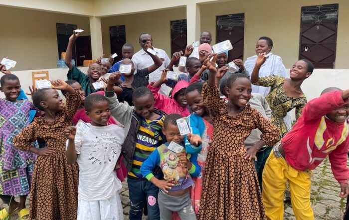 A group of children smile as they hold up their new government health insurance cards.