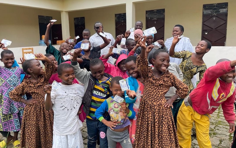 A group of children smile as they hold up their new government health insurance cards.